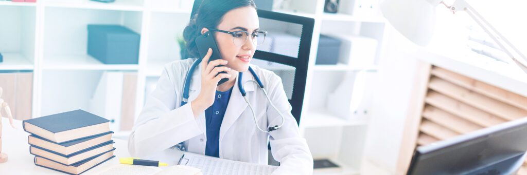 A charming young girl with glasses, a blue blouse and a white robe is sitting in the office. A stethoscope hangs around her neck. photo with depth of field. 9 Telephone Triage Red Flags