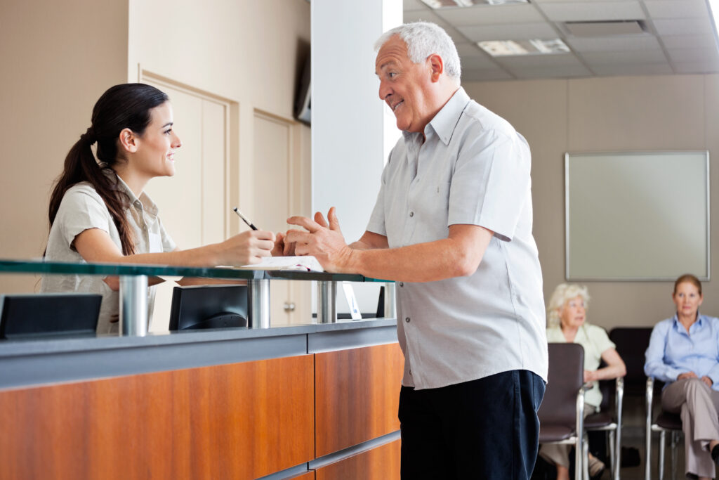 Senior man communicating with female receptionist while women sitting in background. 9 Telephone Triage Red Flags