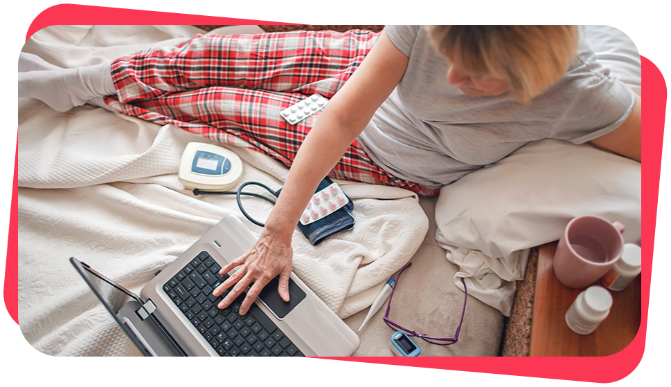 A person in pajamas lays beside monitoring equipment while using their laptop.